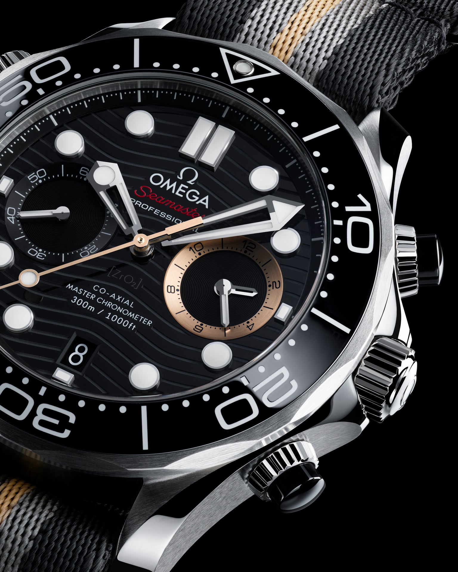 Omega Seamaster Diver chronograph with black dial, white hour markers, rose gold subdial, and black fabric strap.