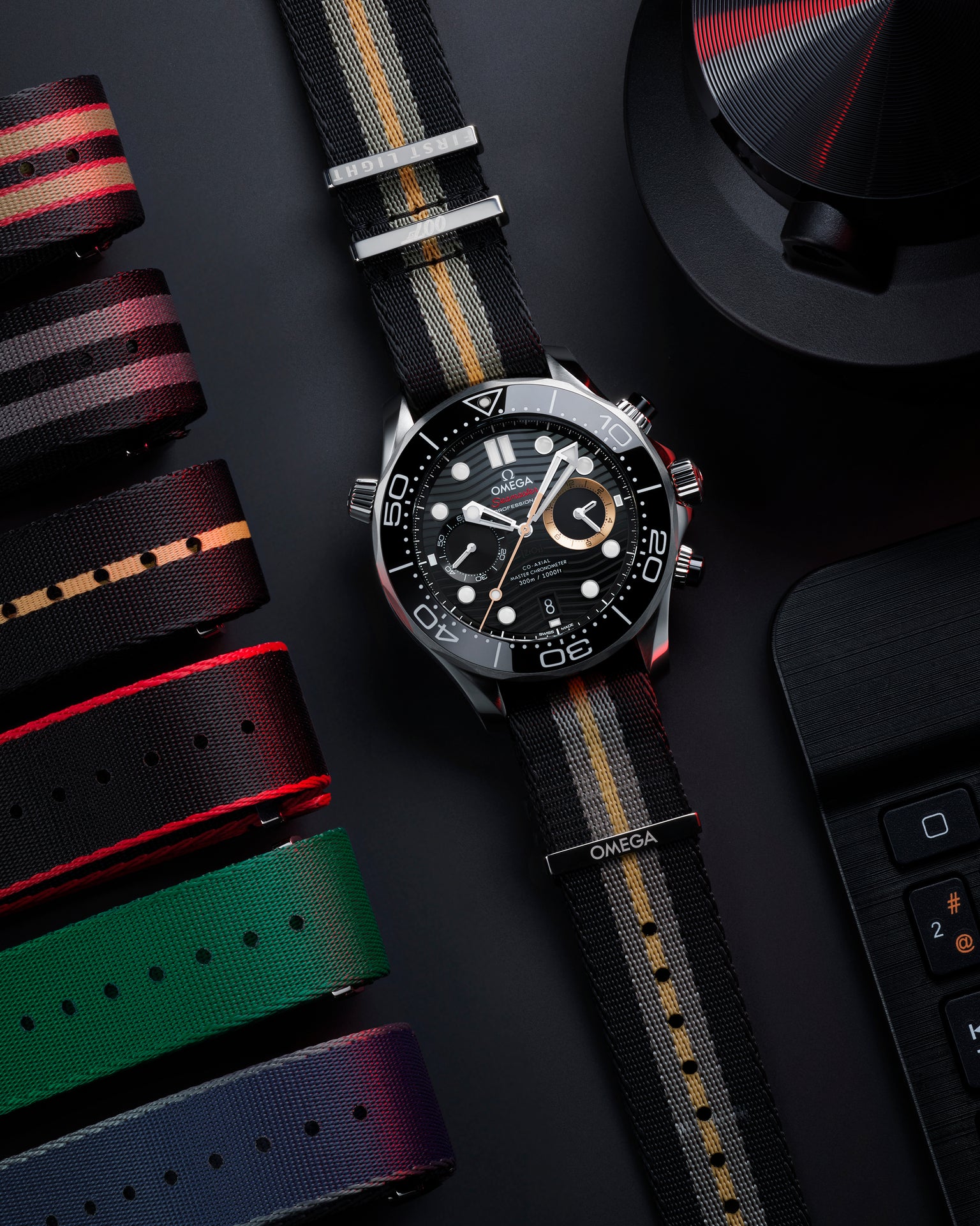 Stainless steel chronograph watch with black dial, white hour markers, and striped fabric strap with red and gold accents.