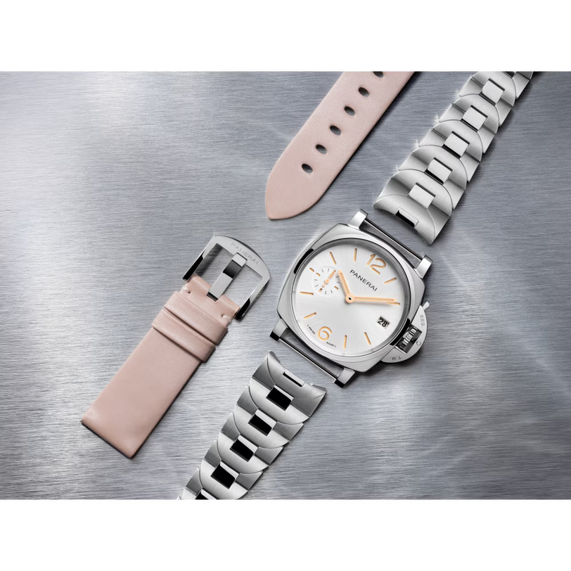 The Panerai Luminor Due, a silver wristwatch with a white and gold face, P.900 automatic movement, and 3-day power reserve, is shown on a brushed metal surface beside a beige leather strap and matching buckle.