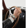 A person wearing a Timex Marlin® Chronograph Tachymeter with a large round face grips a vintage wooden steering wheel inside a classic car with a black dashboard.