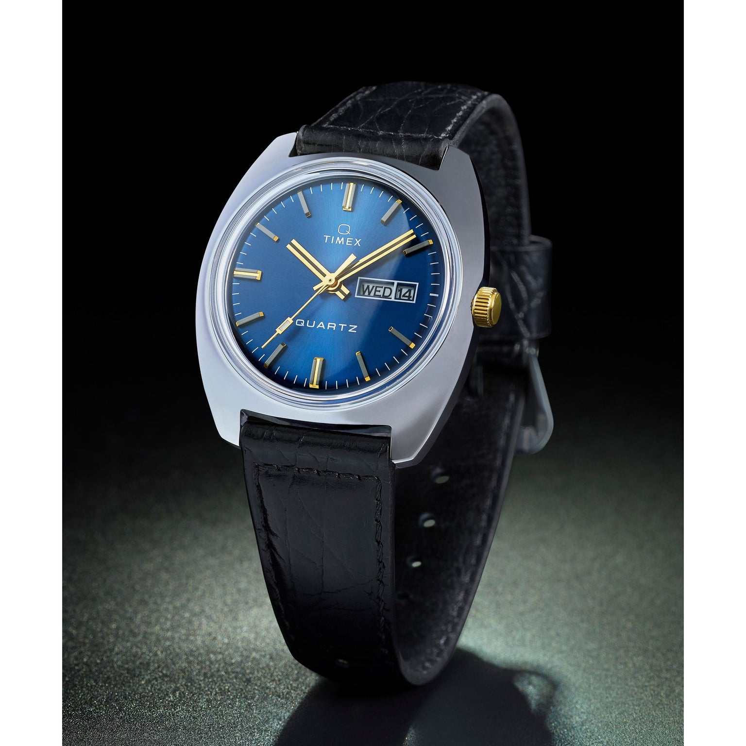 The Timex G SS QZ SW 1978 DAY DTE 37.5 BLU DL 25 is a retro quartz dress watch featuring a blue sunray dial, gold hands and markers, day-date display, silver case, and black leather strap.