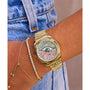 A person in blue denim wears a Timex x Jacquie Aiche watch featuring a gold case, pastel mother-of-pearl dial, and gold-and-diamond bracelet.