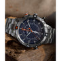 The Timex Expedition Tide-Temp-Compass watch, with its black dial, compass bezel, and orange accents, rests on rough wooden planks. Multiple dials and date display add to its rugged yet refined appeal.