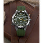 A Timex Expedition® Tide-Temp-Compass analog watch with a green band and black bezel sits on brown leather near thick rope. Its olive-green face features compass markings with white and orange accents.
