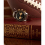 A Timex Waterbury Heritage Chronograph with a stainless-steel case and dark face sits atop an ornate red book, its gold accents gleaming, while an American football appears blurred in the background.