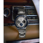 A Timex Q Chronograph watch with a stainless steel bracelet and blue bezel sits on a vintage car dashboard, surrounded by classic dials and a retro radio.
