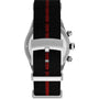 A close-up of the Timex Waterbury Heritage Chronograph shows its black recycled fabric strap with a red center stripe and a silver “TIMEX” buckle. The watch case, tachymeter bezel, and buttons are also partially visible.