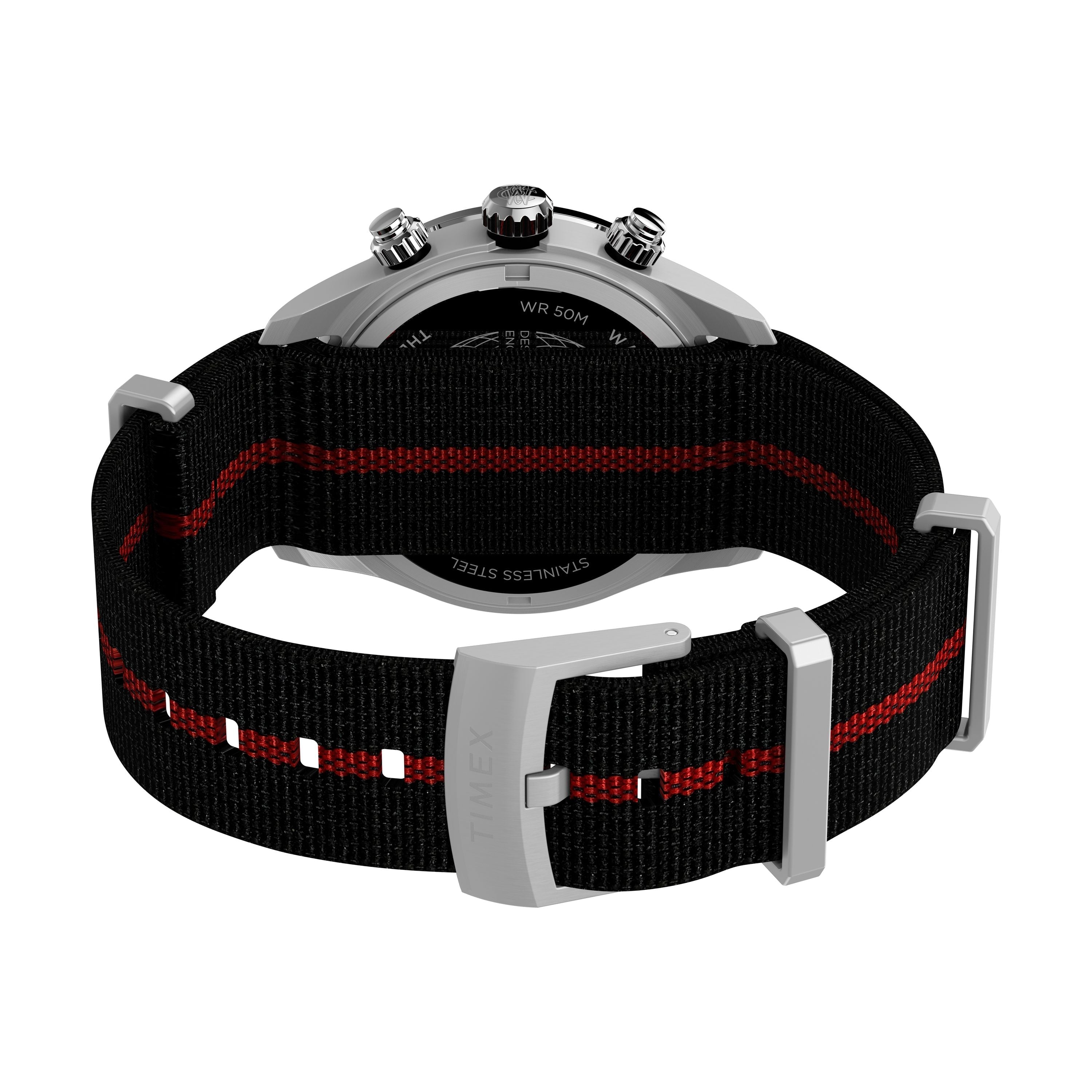 A black and red recycled fabric strap with stainless steel buckle attaches to the back of the Timex G SS QZ WTRBY HERT 39 BLK DL FABR STP 25, revealing its silver chronograph case, visible buttons, and branded details.