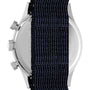 A close-up of the Timex Waterbury Traditional Fly-Back Chronograph shows its stainless steel case partly concealed by a dark blue woven strap, with side buttons and part of the back casing visible.