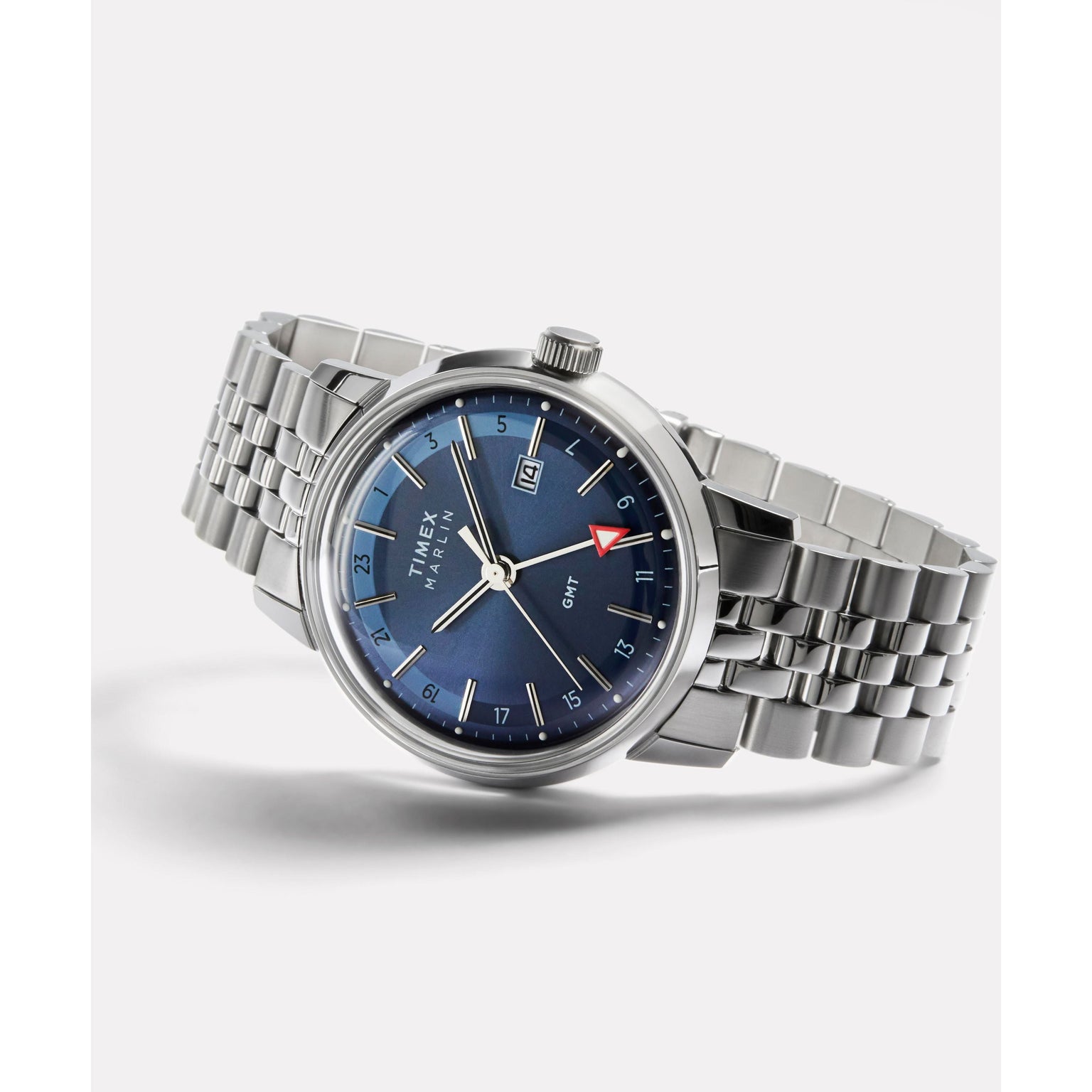 The Timex Marlin® Quartz GMT, featuring a stainless steel case, blue dial, date window, silver markers, and red-tipped GMT hand on a metal bracelet, is shown at an angle against a plain white background.