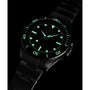 The Timex Atelier Marine M1a Swiss Made Automatic, a black metal wristwatch with luminous green hour markers and hands, glows in the dark. Its minimalist design stands out against a black background, showcasing its modern features.