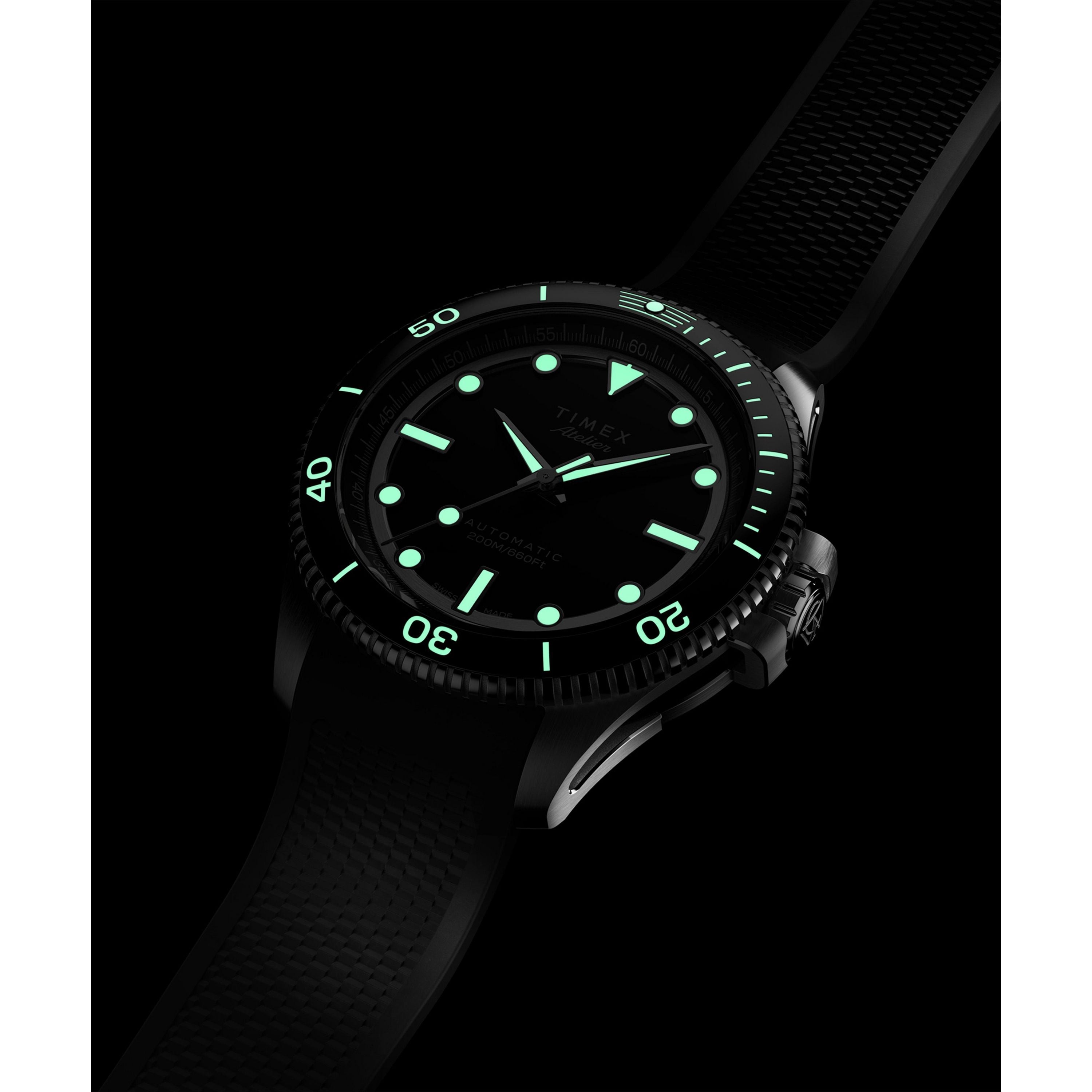 A close-up of the Timex G SS AU SW ATELIER 41 BLACK DL 25 dive watch features luminescent hands and markers glowing green in the dark, shown on a textured black strap, capturing its minimalist and modern tool-watch design.