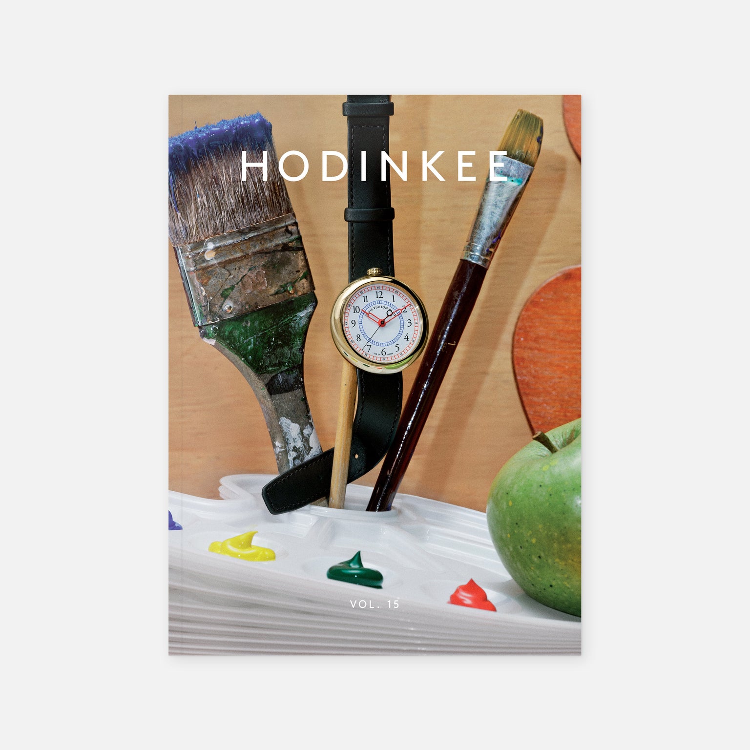 The cover of Hodinkee Magazine Volume 15 by Hodinkee celebrates modern watch culture, showing a paintbrush, wristwatch, and brush in a paint tray next to a green apple, with “HODINKEE” and “VOL. 15.” on the cover.