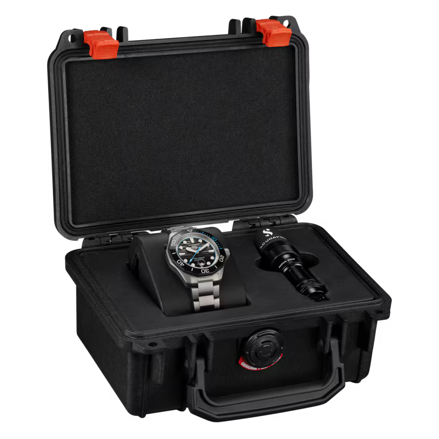 Black rugged case with red latches open to display steel watch with blue dial and black cylindrical object inside.