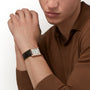 A person in a brown long-sleeve shirt rests their hands together, showcasing the Cartier Tank Louis Cartier Large Model with a white dial, black Roman numerals, and a black leather strap—a true tribute to timeless design.