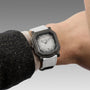 Watch with a gray strap on a wrist, against a neutral background