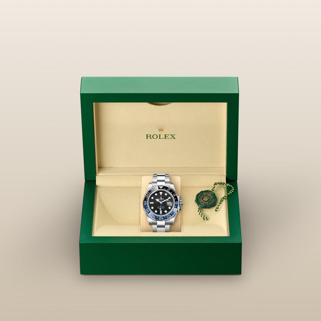 A Rolex watch with a black and blue bezel in a green and beige box with a green tag.