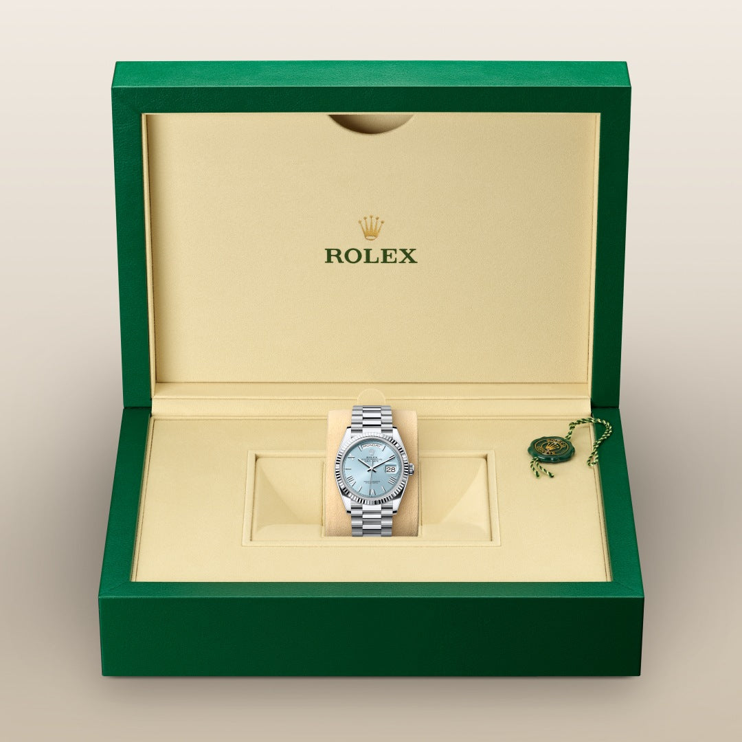 A silver Rolex watch in a green and beige Rolex box with a green tag on the side.