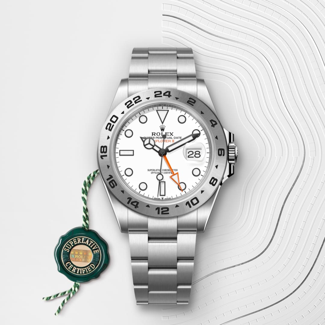 A stainless steel Rolex Explorer II watch with a white dial and orange hand, next to a green Superlative Certified tag.