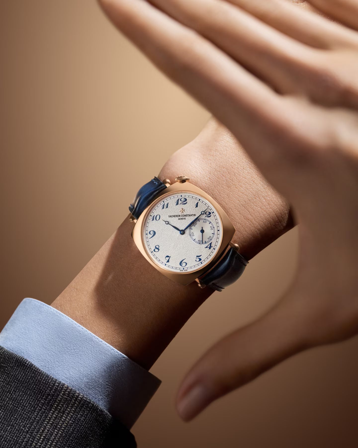 Gold-tone watch with cream dial, blue Arabic numerals, and dark blue leather strap worn on wrist.