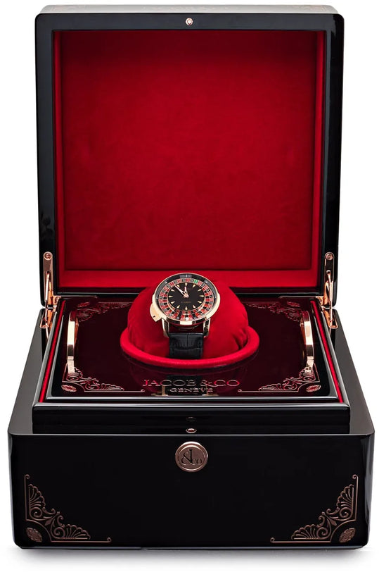 Black watch winder box with red velvet interior displaying tourbillon watch with roulette wheel dial on red cushion.