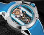 Stainless steel watch with blue dial, exposed gold and black mechanical movement, white hand markers, and blue rubber strap.