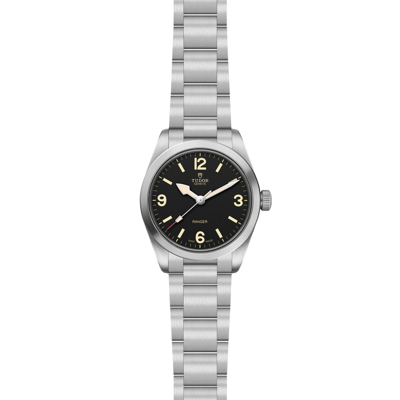The TUDOR Ranger is a stainless steel expedition watch featuring a black dial with prominent numerals at 3, 6, 9, and 12, luminous hour markers, and a silver metal bracelet. The dial is boldly marked "RANGER.