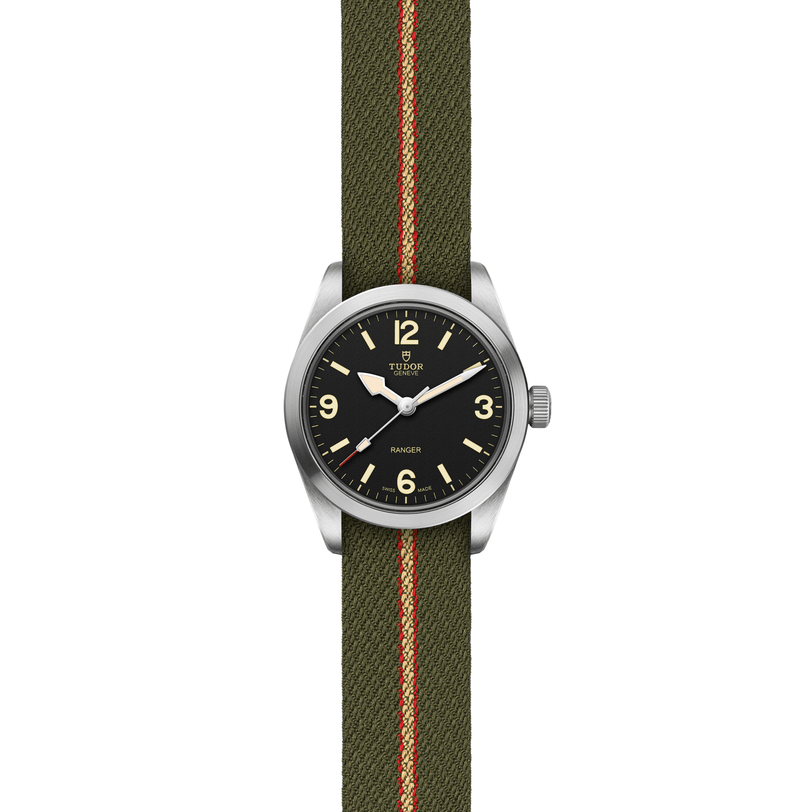 The TUDOR Ranger is a stainless steel expedition watch with a black dial, bold luminescent numerals, and simple hour, minute, and second hands. It comes on a green fabric strap featuring a central red and beige stripe.