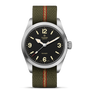 The TUDOR Ranger is an expedition watch with a black dial, large cream numerals and hands, a stainless steel case, and an olive-green fabric strap with a red center stripe.