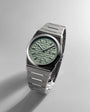Silver watch with a green textured face on a light gray background