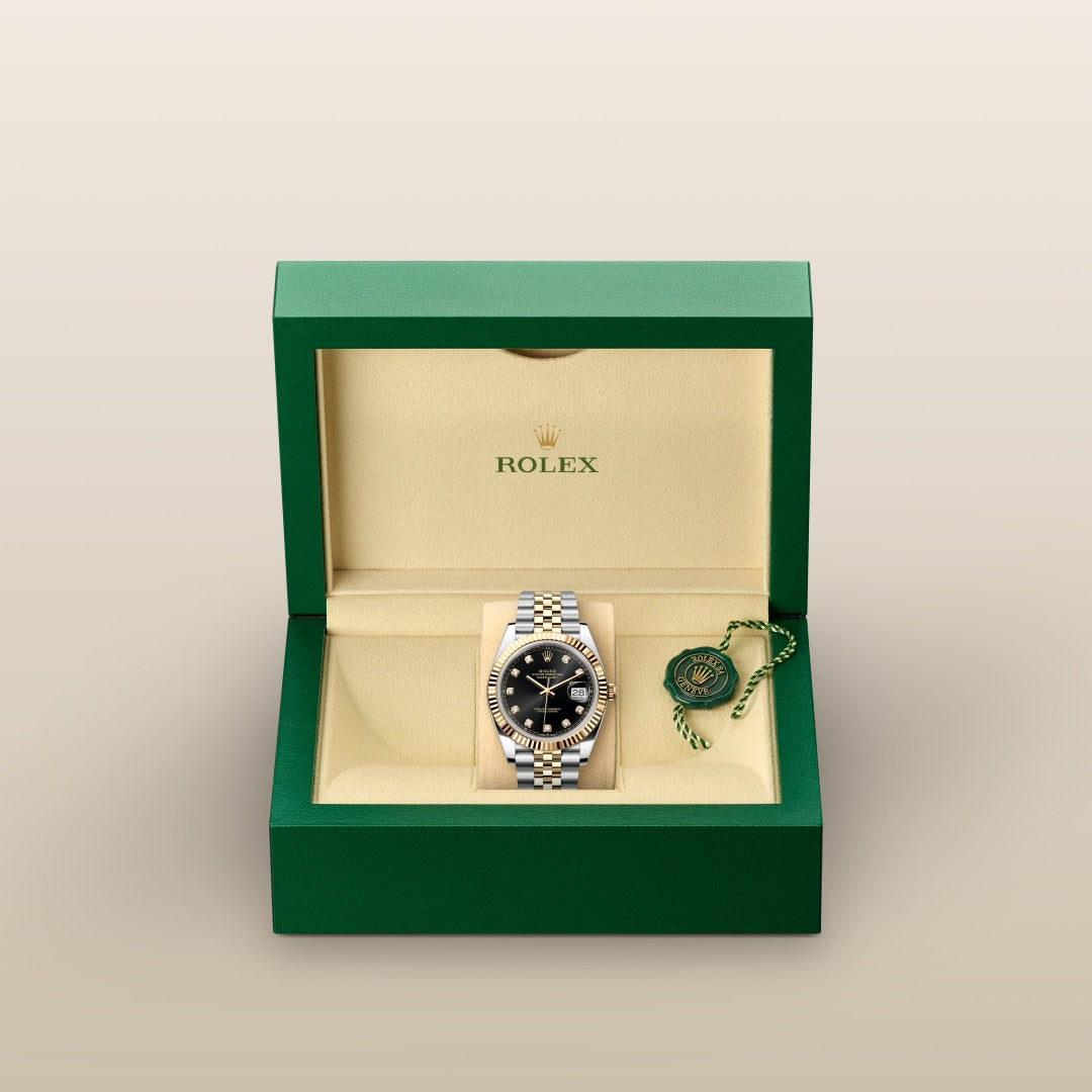A Rolex watch with a black dial in a green and beige Rolex box, next to a green Rolex tag.