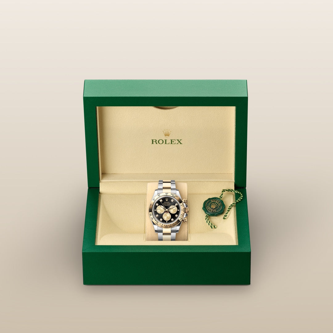 A Rolex watch with a black and gold dial in an open green and cream Rolex box with a green Rolex tag.