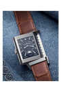 The Jaeger-LeCoultre Reverso Classic Duoface Small Seconds, a rectangular steel luxury watch with a dark patterned dial, silver details, and brown leather strap, sits on blue denim—perfect for tracking two time zones in style.