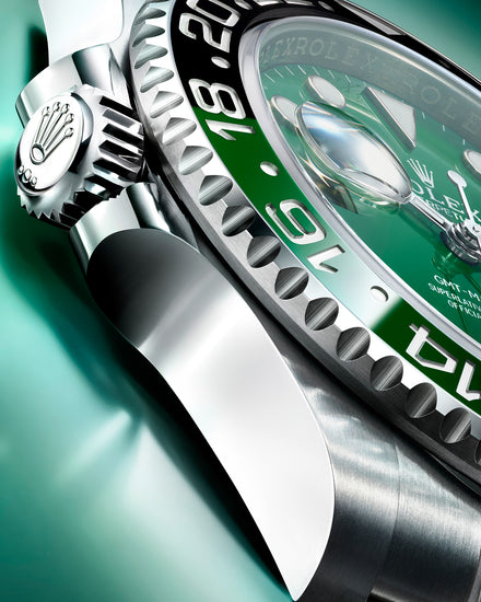 Close-up of a silver and green Rolex GMT-Master II watch on a light green background.