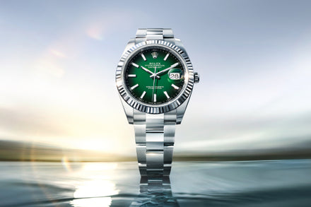 Silver watch with a green face on a reflective water surface with a blurred background