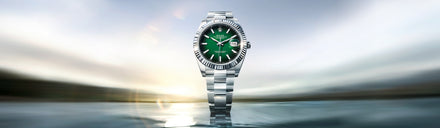 Silver watch with a green face on a reflective surface with a blurred background