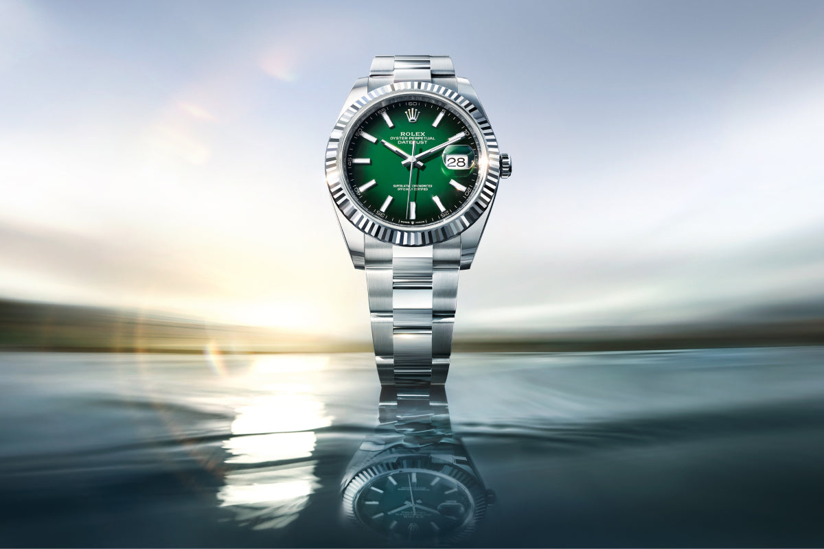 Silver watch with a green face on a reflective surface with a blurred background