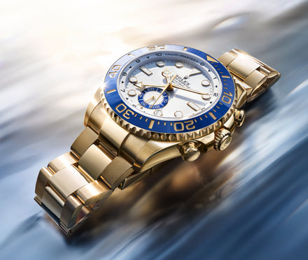 Luxury watch with gold band and blue bezel on a reflective surface