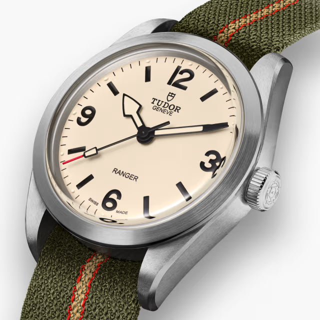 A close-up of the TUDOR Ranger watch featuring a cream dial, bold black numerals and hands, and a green fabric strap with an orange stripe. Its brushed and polished stainless steel case ensures durability and timeless style.
