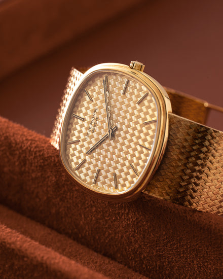 A gold wristwatch with a textured zigzag pattern on the dial and band, resting on a brown surface.